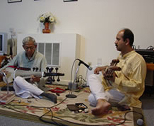 Two men sitting on a rug playing music instruments.