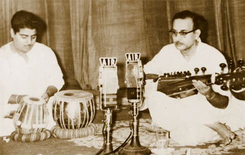 Two men sitting on the floor playing musical instruments.