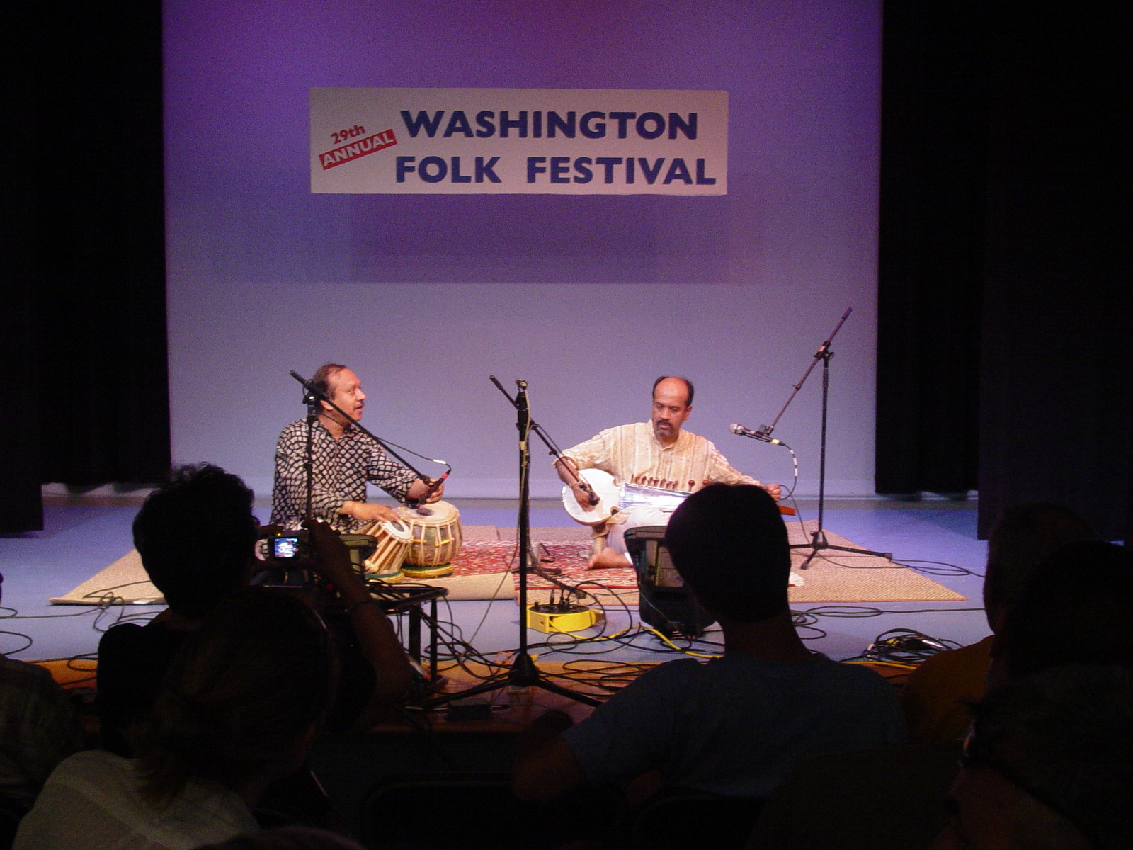 Two men sitting on stage playing instruments and singing.