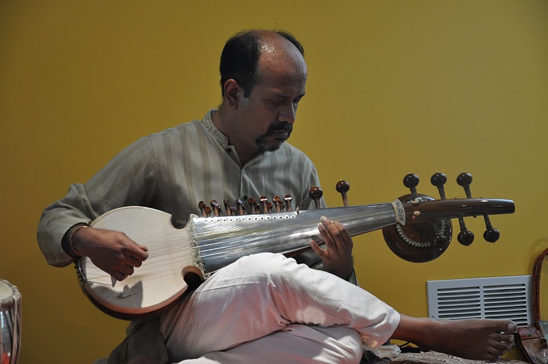A man playing an instrument while another person sits on the floor.