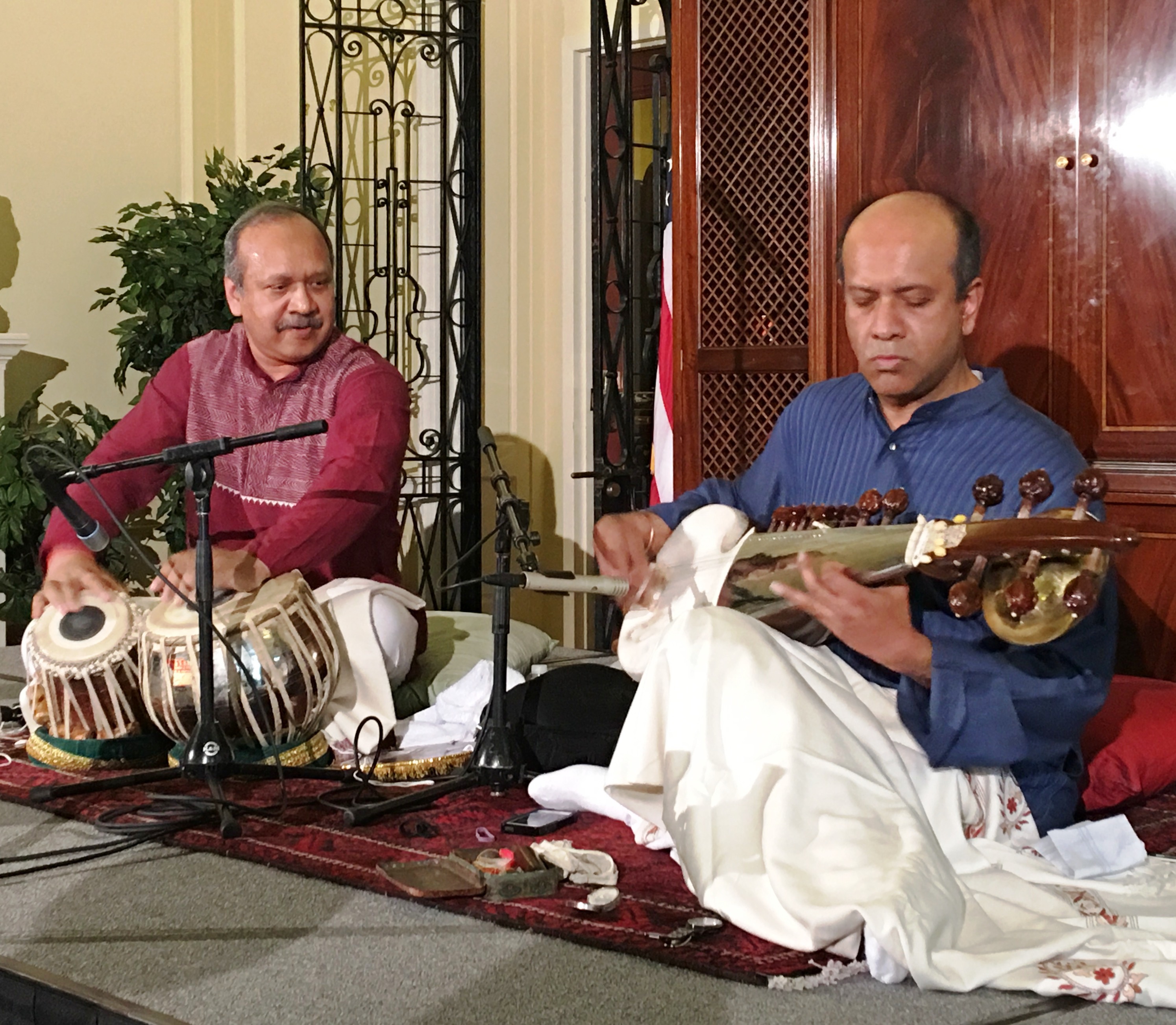 Two men sitting on a floor playing musical instruments.