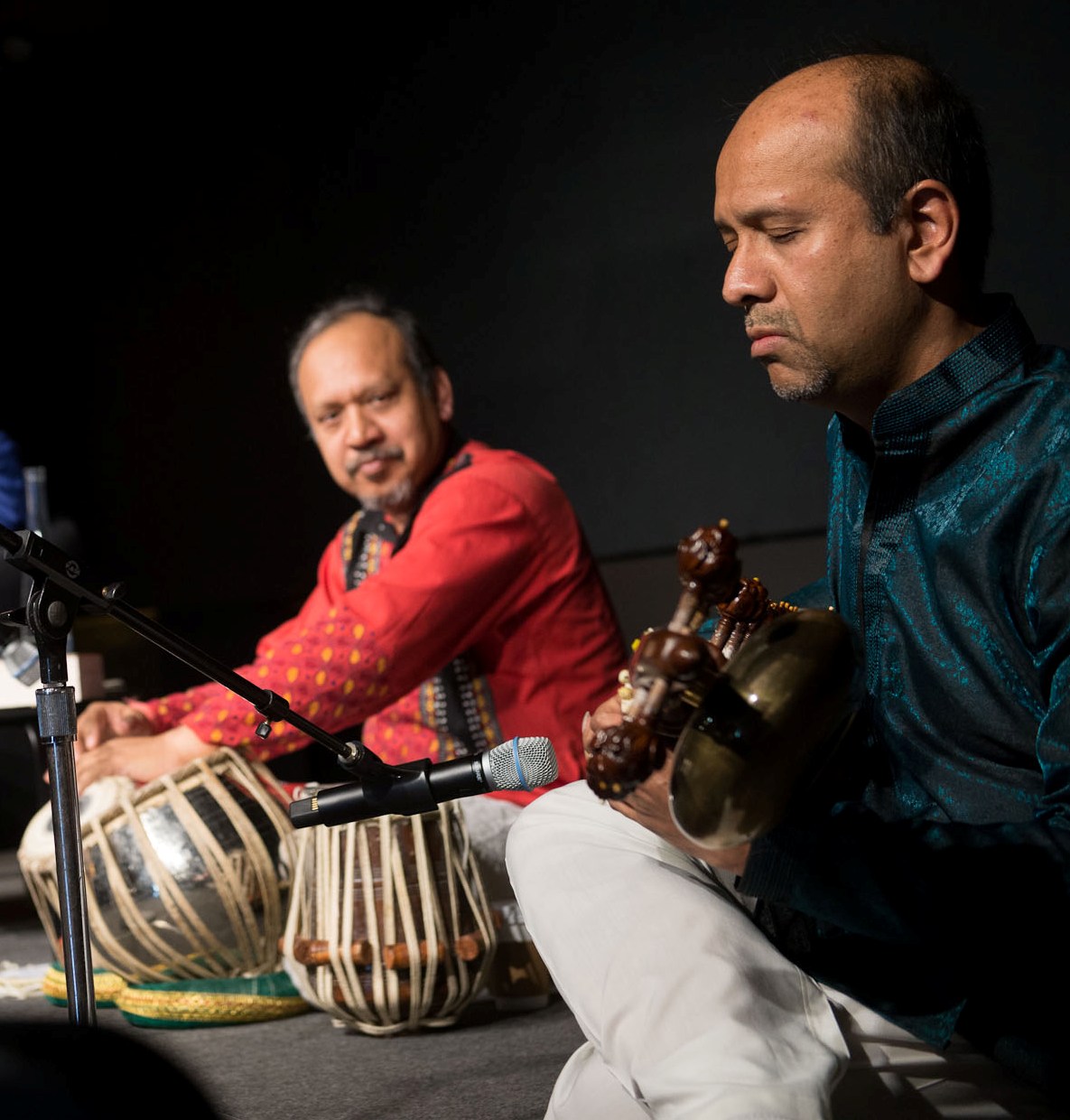 Two men sitting on a stage playing musical instruments.